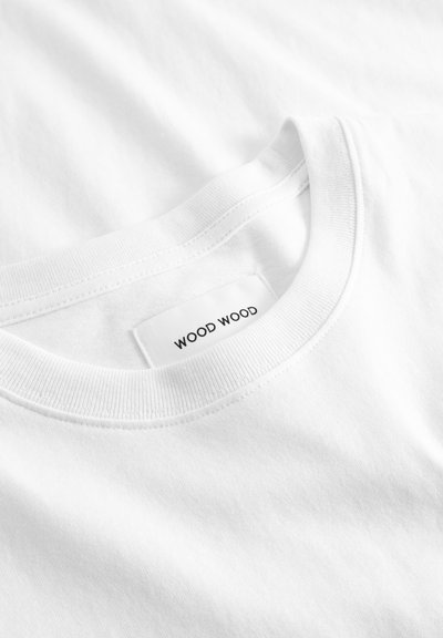 Nærbilde av en hvit crewneck-T-skjorte som viser sydd halslinning og merkeetiketten "WOOD WOOD" inni halsåpningen.