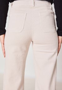 Lichtbeige wijde corduroy broek met verticale ribbels, voorzien van twee achterzakken en een hoge tailleband. Geweven stof, relaxte pasvorm.