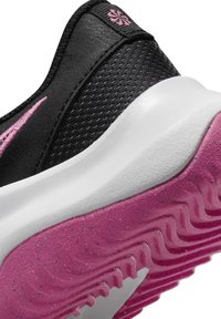 Černá sportovní bota s růžovým švihem a texturovanou růžovou podrážkou, s prodyšným síťovaným svrškem a bílou polstrovanou mezipodrážkou.