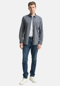 Herren-Karohemd zum Knöpfen in Grau, Regular Fit, langärmlig, mit Brusttasche, kombiniert mit blauen Jeans und weißen Sneakern.