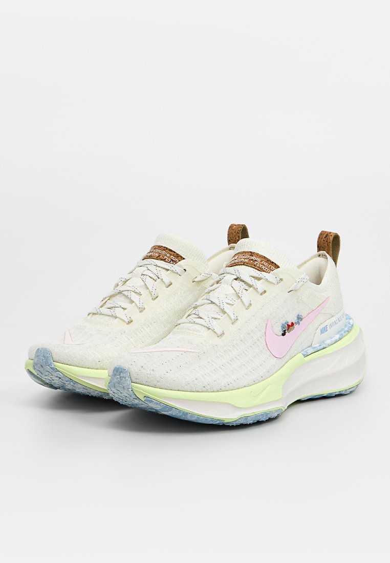 Zapatillas de correr Nike con una parte superior texturizada en crema claro, acentos en rosa, una suela acolchada con detalles en menta y azul, y etiquetas de logo marrón.