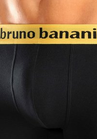 Mustat boxerit, joissa on keltainen elastinen vyötärölautan, jossa on brändin nimi "bruno banani" mustalla tekstillä. Pehmeä kangas, joka muotoilee vartalon.