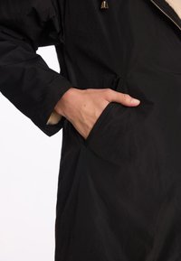 Czarna wodoodporna kurtka z zamkiem z przodu, miękkim wykończeniem i bocznymi kieszeniami. Gładka tekstura z minimalistycznym designem i złotymi detalami.