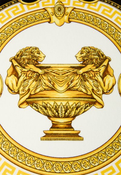 Εκλεπτυσμένο χρυσό μπολ με δύο λιοντάρια που κρατούν υφασμάτινη επιφάνεια, περιβαλλόμενο από περίπλοκα κυκλικά διακοσμητικά μοτίβα σε λευκό φόντο.