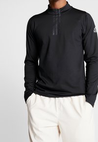 Schwarzes, langärmliges Sportoberteil mit hohem Kragen, das drei vertikale Streifendetails auf der Brust und eine glatte, strukturierte Oberfläche aufweist.