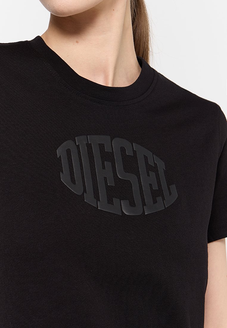 Primo piano di una persona che indossa una maglietta nera con un grande logo in rilievo Diesel sul petto, ritagliato sotto il naso e sopra la vita.