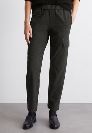 Dunkelgrüne, strukturierte, schmal zulaufende Hose mit elastischem Bund und seitlicher Cargo-Tasche, kombiniert mit schwarzen Schuhen. Geeignet für Freizeitkleidung.