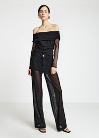 Haut noir épaules dénudées avec tissu froncé, associé à un pantalon large noir transparent avec un détail de boutons sur le devant. Des sandales élégantes complètent la tenue.