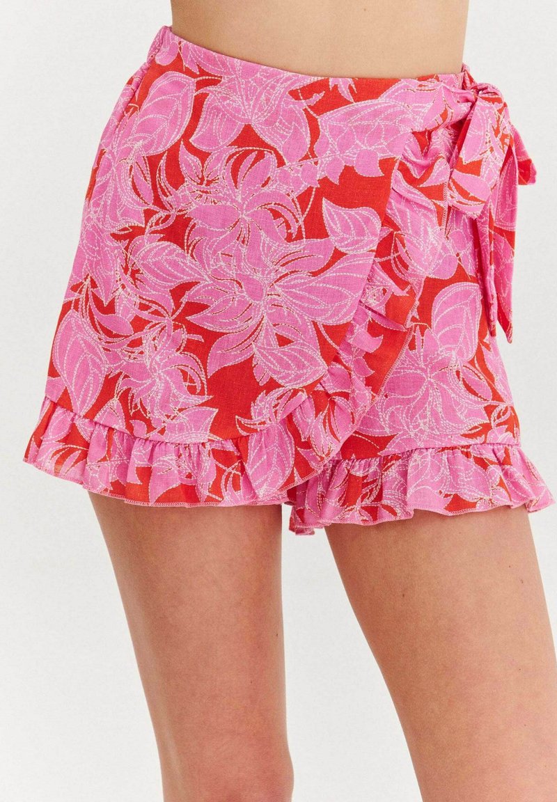 Kvetinová sukňa so zavinovaním v červenej farbe s ružovými listovými vzormi, s volánovým lemom a viazaním v páse. Vyrobená z ľahkej látky.