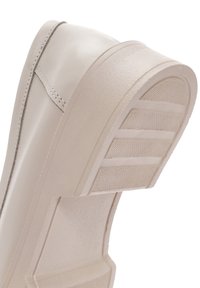 Sneakers beiges avec une tige en cuir lisse et une semelle en caoutchouc texturée. Présente un accent cousu discret et un embout arrondi.
