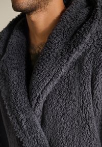 Donkergrijze fleecebadjas met een gestructureerd, pluizig oppervlak, voorzien van een brede kraag en revers, die de schouders en het bovenste borstgebied bedekt.