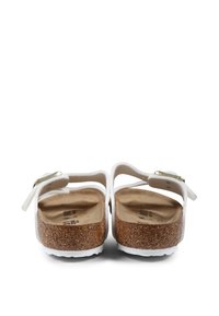 Sandales blanches avec deux sangles ajustables, semelle en liège et semelle en caoutchouc texturé. Des accents en métal doré sont visibles sur les sangles.