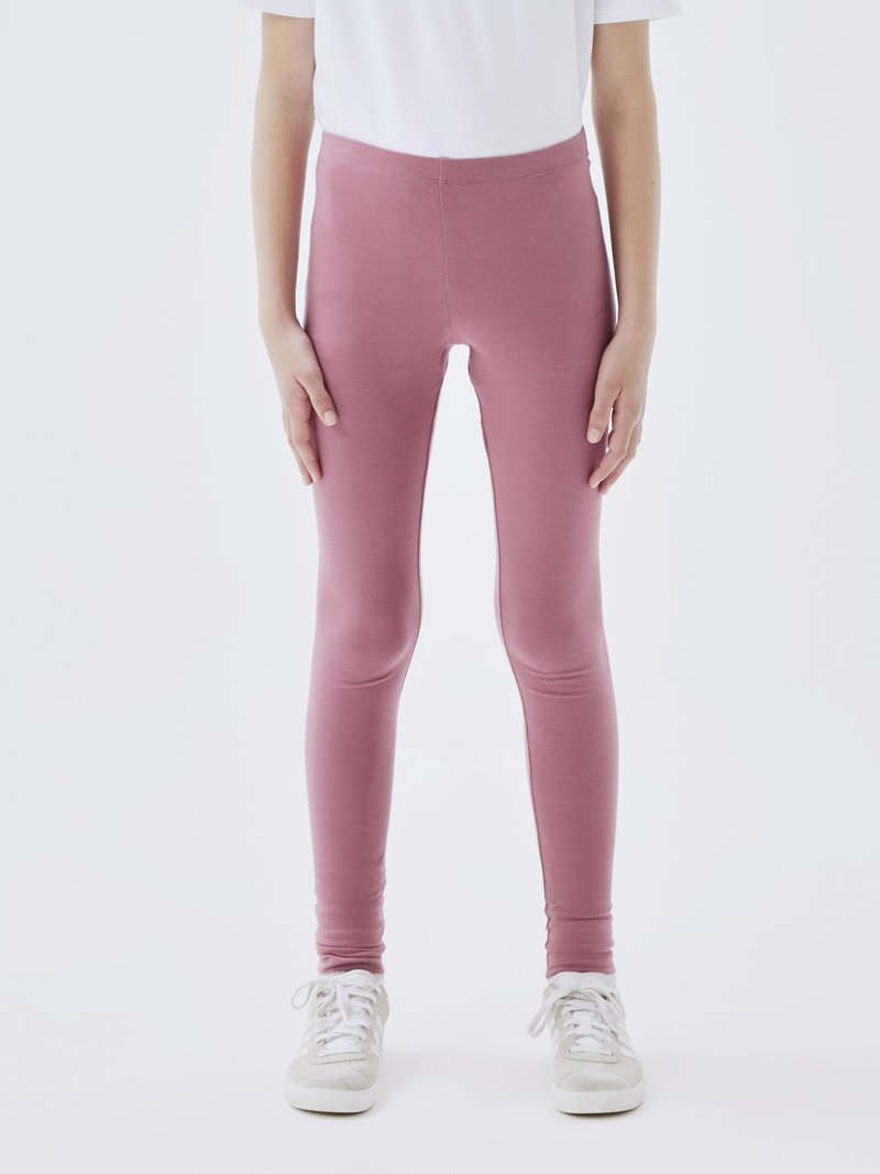 Leggings roses fabriqués en tissu extensible, dotés d'une taille haute et d'une texture lisse. Associés à des baskets blanches.