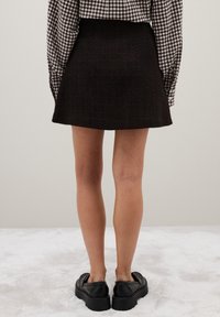 Minifalda de tweed negro con acabado texturizado, combinada con una camisa a cuadros y zapatos negros de plataforma, vista desde atrás.