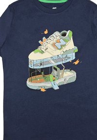 T-shirt blu navale con una grafica di una sneaker bianca e verde, con scene sportive dettagliate rappresentate all'interno e attorno ad essa.