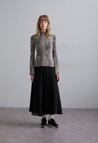 Maglietta a maniche lunghe con motivo a zigzag bianco e nero, abbinata a una gonna plissettata nera e scarpe da ginnastica nere. Texture liscia con design aderente.