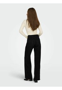 Sorte bredbenede jeans med høj talje, der har baglommer og kontrastsyninger. Sammen med en cremefarvet langærmet top.