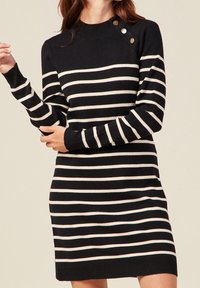 Robe en tricot à rayures noires et blanches avec un col ras du cou et des accents de boutons sur l'épaule, dotée de manches longues et d'une silhouette ajustée.