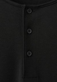 Tissu tricot noir avec une patte de boutonnage à l'avant comportant trois boutons noirs ronds et des coutures visibles le long de l'encolure et de la zone des boutons.