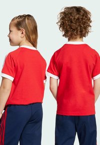 Red short-sleeve T-shirt made of cotton, featuring a white collar and cuffs, worn by two children viewed from the back.
