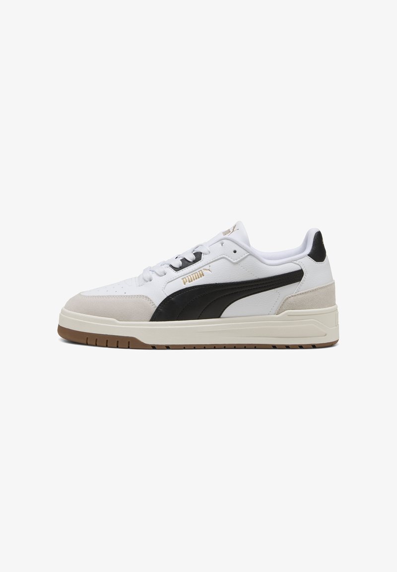 Baskets blanches avec des accents noirs et beiges, en cuir et daim, semelle en caoutchouc plate, et logo PUMA en or sur le côté.