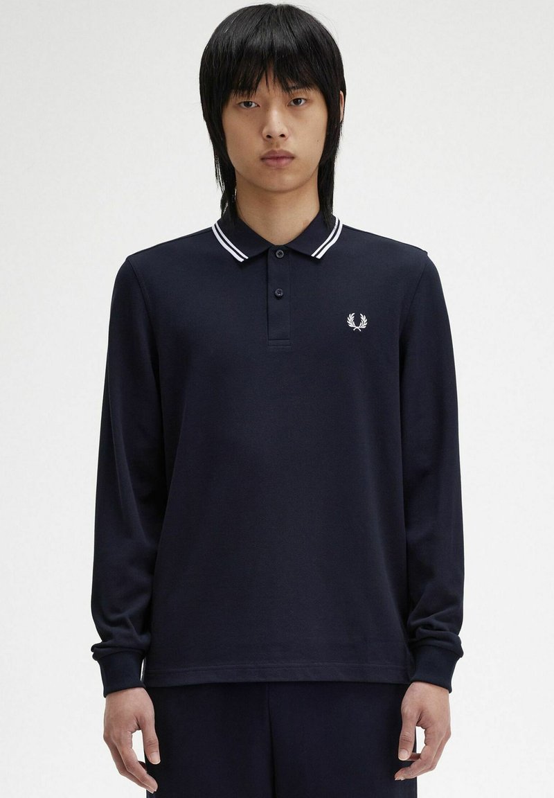 Polo a maniche lunghe di colore blu navy con colletto e polsini bianchi a contrasto, dotato di un piccolo logo bianco sul lato sinistro del petto. Tessuto di texture liscia.