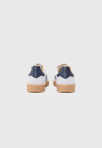 Vita och marinblå sneakers med övre i mocka, en gummisula och ett vågformat mönster på hälen. Har varumärkesdetaljer på baksidan.