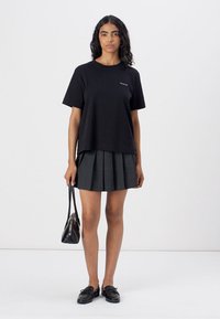 T-shirt nera a maniche corte con vestibilità comoda e piccolo logo, abbinata a una gonna grigia a pieghe, borsa nera e mocassini neri.