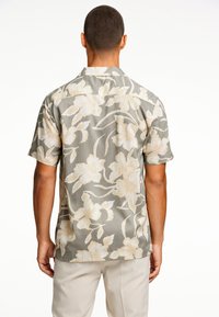 Camisa de manga corta con estampado floral en gris apagado y flores beige, con cuello y un corte relajado. Diseño de tela texturizada.