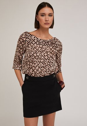 Blusa nera trasparente con pois rosa e bianchi, con scollo a barca e maniche tre quarti; abbinata a una mini gonna nera avvolgente con bottoni.