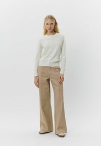Beige brede benbukser parret med en cremefarvet cardigan med knapper. Cardiganen har en rund halsudskæring og let tekstur. Sættet er iført med flade sko.