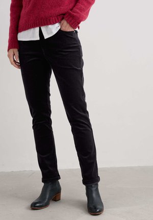 Pantaloni negri din corduroy cu croi slim, având cinci buzunare și mansete răsucite, asortați cu un pulover tricotat roșu și cizme negre până la gleznă.