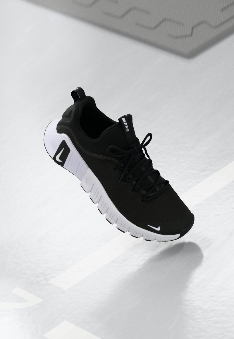 Black athletic shoe with a textured black upper, white sole, and prominent black laces. Features a tab on the heel and branding on the side.