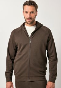 Felpa con zip marrone realizzata in un tessuto morbido e strutturato. Presenta un cappuccio, maniche raglan e polsini a costine. Dettaglio della zip argento molto evidente.