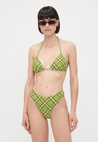 Bikini-set med ett grönt, gult och svart rutig mönster. Triangeltopp med justerbara snören; högskurna botten med liknande mönster.