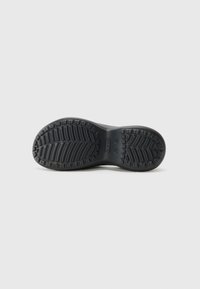 Semelle de chaussure noire avec des motifs de bande de roulement profonds et le nom de la marque embossé au centre, présentée sur un fond clair uni.