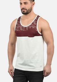 Herre tanktop i hvid med en maroon, blomsterpræget øverste sektion og en brystlomme. Lavet af blødt stof, har den en afslappet pasform og brede stropper.