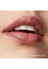 Lippenfarbe in einem sanften Nude-Pink-Ton, glatte Textur mit einem matten Finish, das gut definierte Lippen und sichtbare Zähne betont.