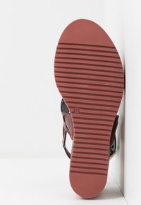 Semelle de sandale rouge avec des rainures horizontales, pressée contre un mur blanc, affichant la pointure "37" près de la voûte plantaire.