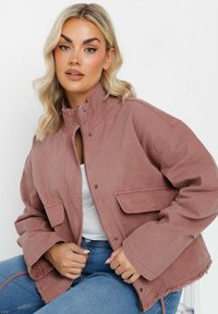 Rosa kordjacka med hög krage, framdragkedja och två bröstfickor; har fransad nederkant och avslappnande passform på ärmarna.