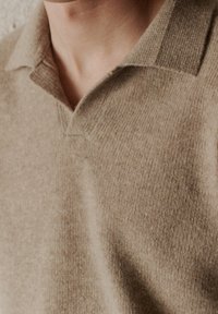 Gros plan d'une personne portant un pull beige en tricot avec un col et un décolleté en V.