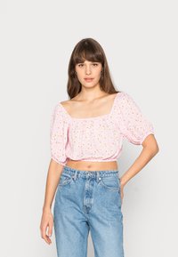 Blusa rosa curta com mangas bufantes, apresentando um decote quadrado e um pequeno padrão floral. Combinada com jeans de cintura alta.