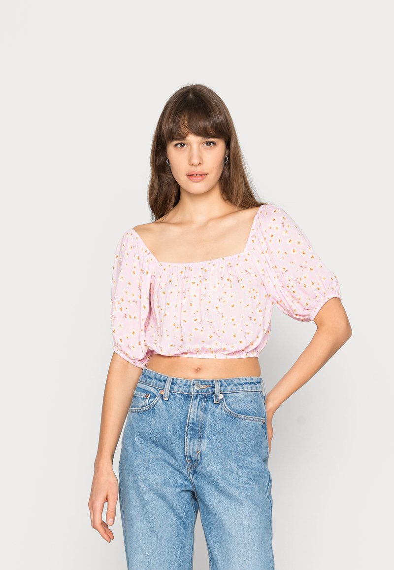 Blusa rosa curta com mangas bufantes, apresentando um decote quadrado e um pequeno padrão floral. Combinada com jeans de cintura alta.