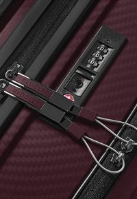 Valigia texturizzata bordeaux in primo piano che mostra le doppie cerniere con "REDOLZ" e serratura a combinazione TSA integrata.