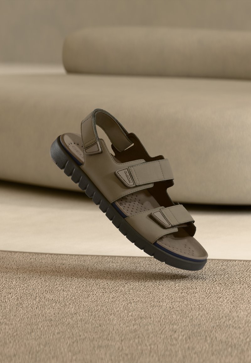 Μπεζ σανδάλι με δύο ρυθμιζόμενις λουριά, καουτσούκ σόλα και διάτρητη εσωτερική σόλα, με υφή και μινιμαλιστικό σχεδιασμό.