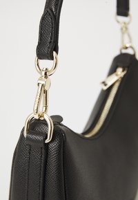 Black leather handbag featuring a textured finish, gold hardware, a zip closure, and a detachable strap with a clip attachment.