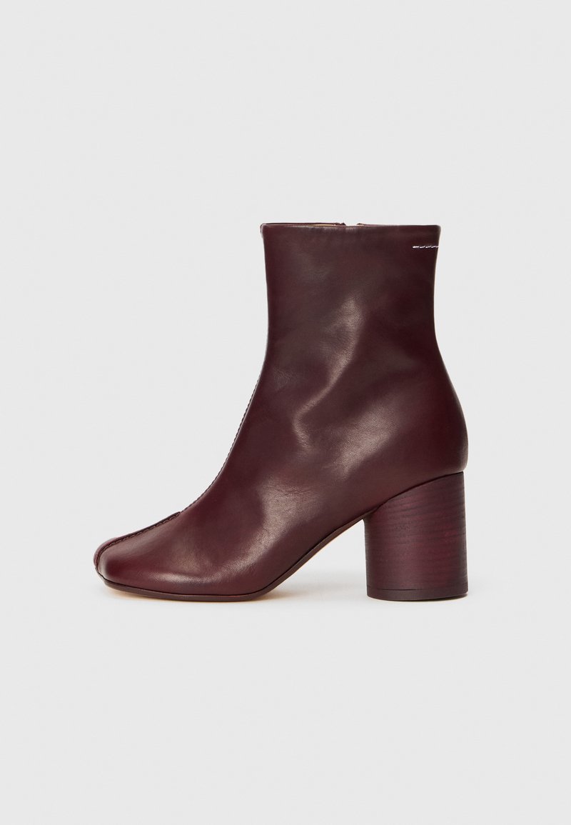 Botín de cuero burdeos con punta redonda, textura suave y tacón ancho, que cuenta con un cierre de cremallera en la parte trasera.