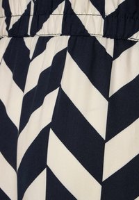 Tummansinisestä ja kermasta kangasta, jossa on chevron-kuvio. Materiaali on teksturoitu, ja siinä on kerrottu vyötäröyksityiskohta, mikä luo erottuvan muotoilun.