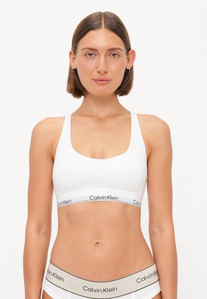 Sostenitore sportivo bianco con spalline larghe e scollo a barca, con il logo nero "Calvin Klein" sull'elastico. Materiale liscio ed elastico.