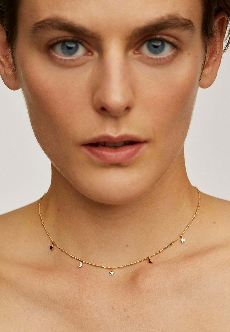 Collar de cadena de oro con pequeños charms de estrella y luna creciente, que presenta un diseño delicado y una textura suave.